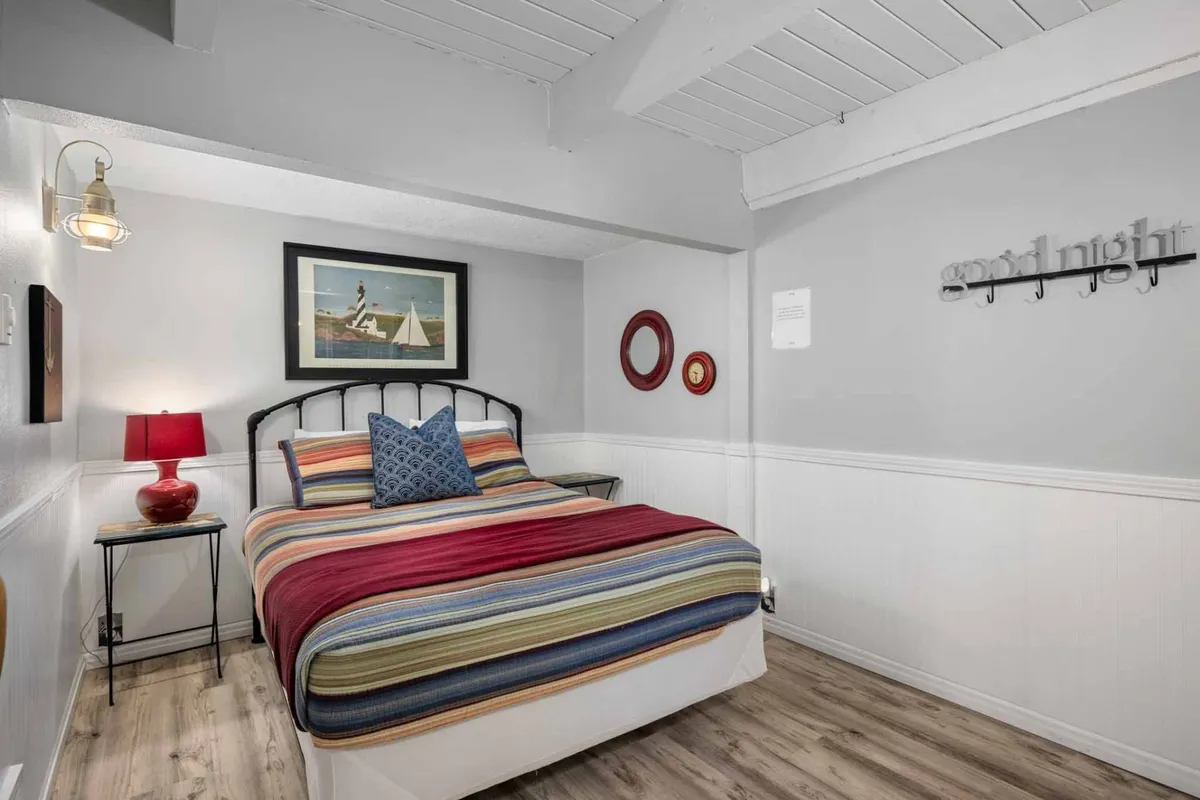 A welcoming bedroom with a striped bedspread, red lamp, framed artwork, decorative mirrors, and a whimsical 'good night' sign. The décor is inviting, offering a cozy and comfortable space for guests.