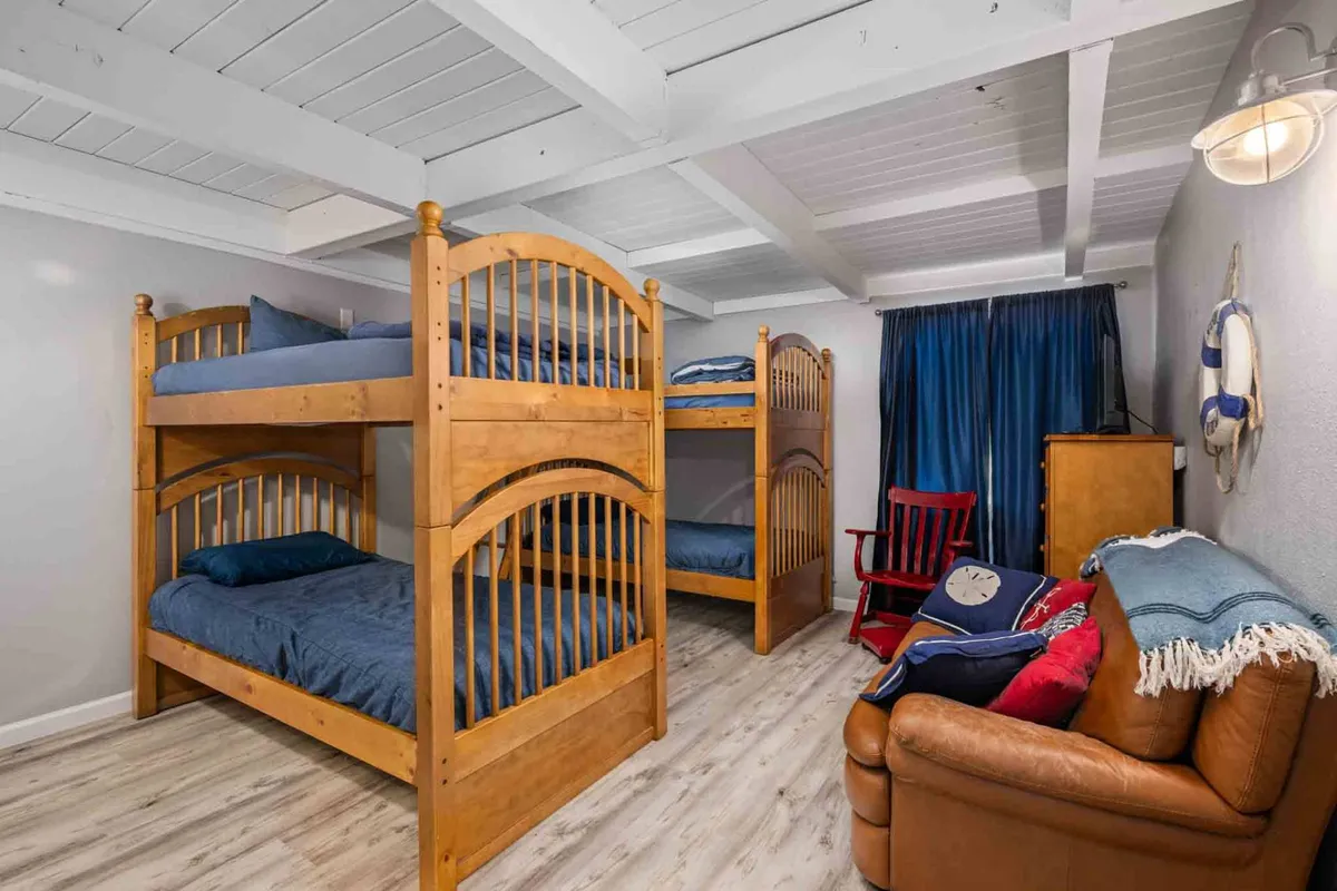 A playful, kid-friendly bunk room with colorful bunk beds, a red rocking chair, and blue curtains. The space exudes a sense of fun and relaxation, ideal for children to enjoy sleepovers and imaginative play.