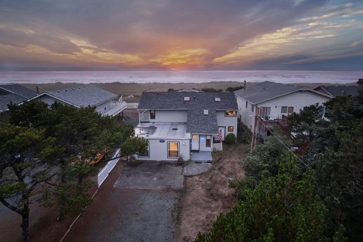 This exterior shot captures the house in the foreground with a stunning sunset over the ocean and surrounding trees, highlighting the direct access from the home to the beachfront. The peaceful mood emphasizes the easy transition from indoor family time to outdoor play and sunset gatherings.