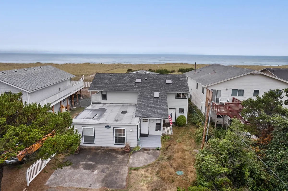 This exterior view presents the house nestled among surrounding greenery with the ocean stretching out beyond. It suggests easy access to the beach for outings and shows a tranquil environment for family gatherings and relaxation, including sunset views from the porch.
