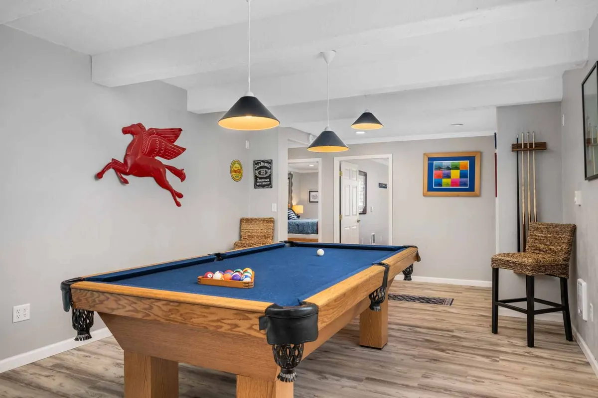This inviting interior features a tastefully designed entertainment space anchored by a pool table, accented by bold red horse wall art, stylish pendant lighting, and bar stools. The setting encourages guests to socialize, entertain, and unwind in a space where design and hospitality meet.