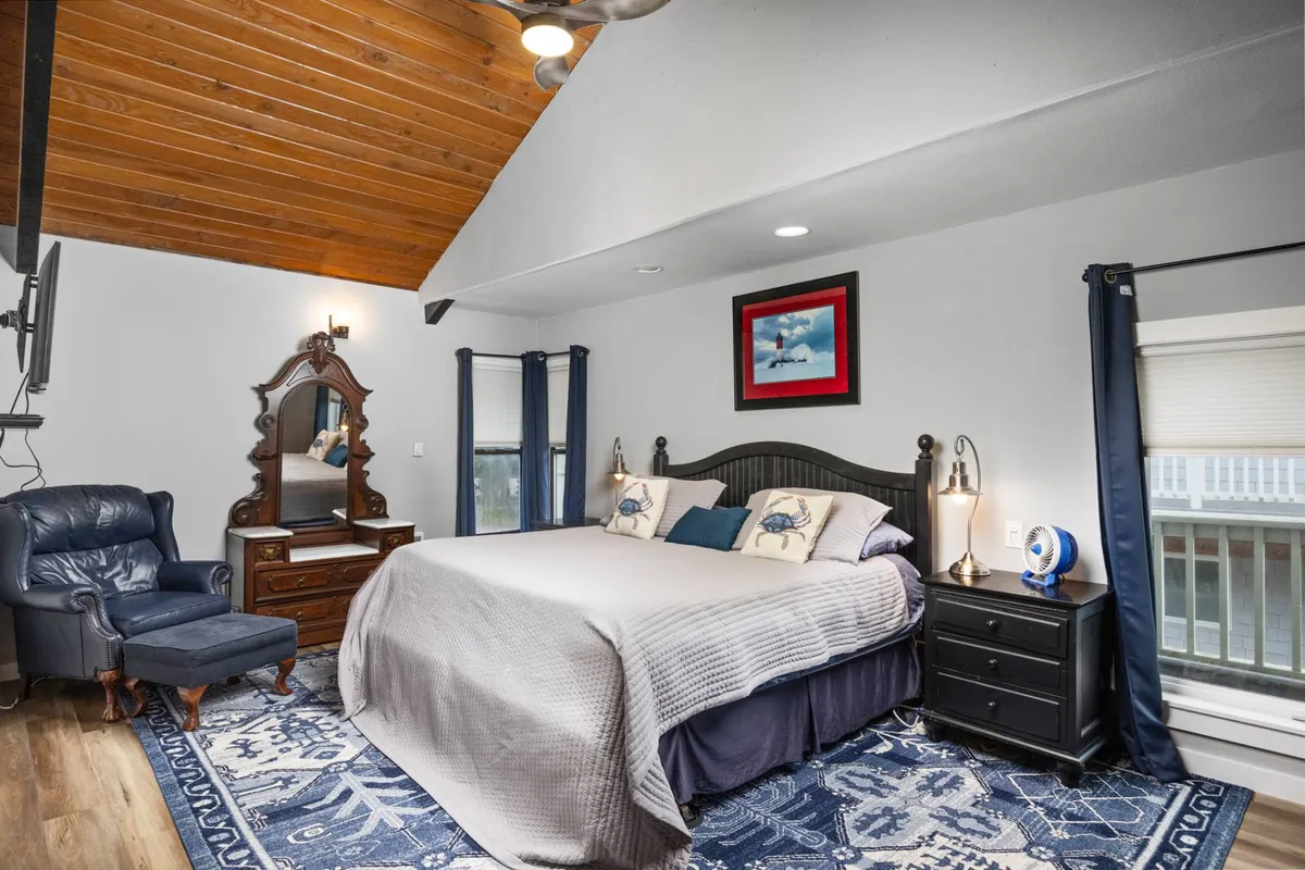 A tranquil bedroom featuring a plush bed draped in soft bedding, a cozy rug underfoot, a stylish mirror, and elegant artwork on the wall. Natural light filters in, highlighting the serene and restful atmosphere of the space.
