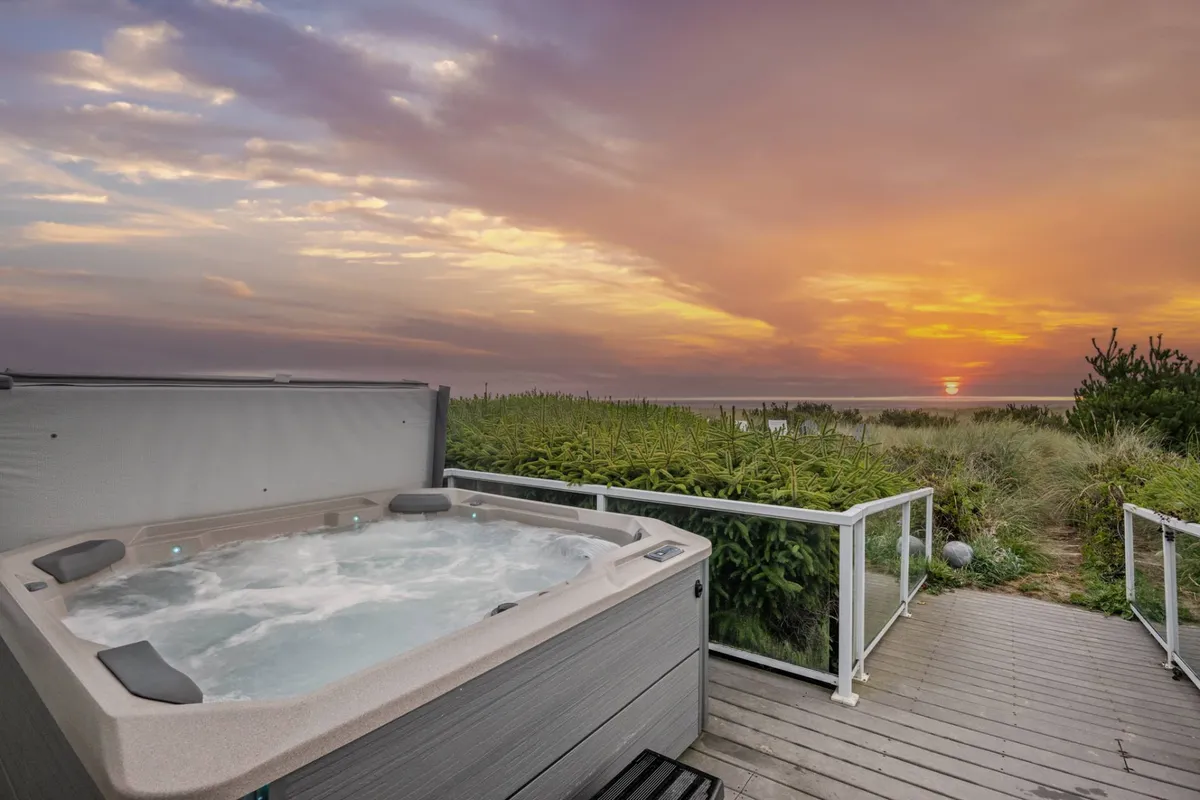 An outdoor setting featuring a hot tub at sunset with panoramic ocean views, where friends are relaxing, sharing a toast, and enjoying the serene ambiance and ocean breeze.