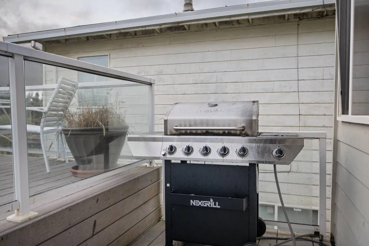 This image shows a spacious wooden deck with a barbecue grill and a planter, suggesting a welcoming space for outdoor cooking and socializing. The deck is designed for relaxation and entertaining, providing ample room for group gatherings.