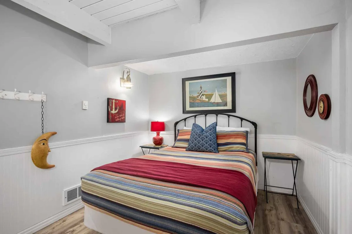 A cozy bedroom with a striped bedspread, blue accent pillows, framed artwork, a red bedside lamp, and a whimsical moon decoration. The setting feels welcoming and comfortable, perfect for relaxation after active days outdoors.