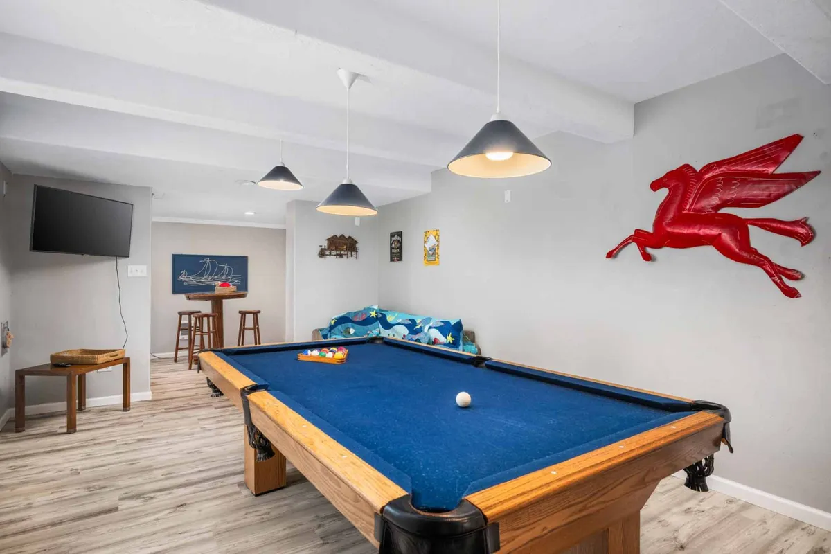 A vibrant game room with a pool table as the centerpiece, colorful Pegasus wall art, a plush sofa with lively cushions, and a TV. The space is inviting, set up for friendly matches, movie marathons, or relaxing with friends.